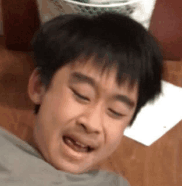 a young boy laying on a wooden table with his eyes closed and his mouth open