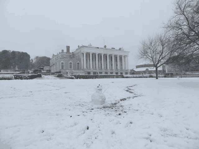 a snowman in front of a large building in the snow