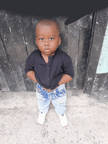 a little boy with his hands on his hips stands in front of a black wall