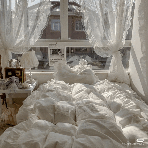 a bed with white sheets and pillows in front of a window with a sign that says the graduate