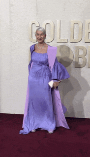 a woman in a purple dress is standing on a red carpet in front of a wall that says gold