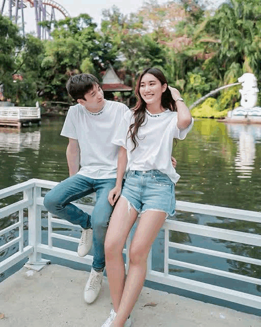 a man and a woman are sitting on a railing near a lake