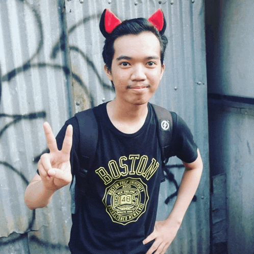 a young man wearing devil horns and a boston shirt