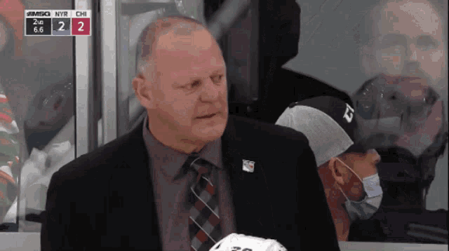 a man in a suit and tie sits in the stands watching a hockey game between the nyr and chi