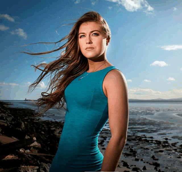 a woman in a blue dress is standing on a beach