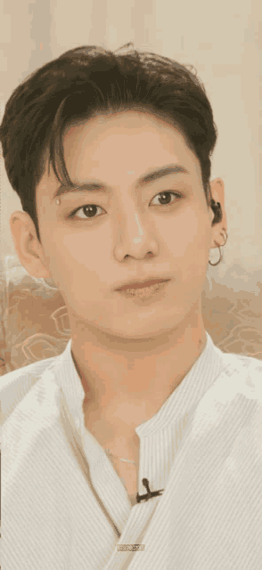 a close up of a young man 's face with a white shirt and earrings