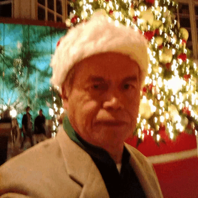 a man wearing a white santa hat stands in front of a christmas tree