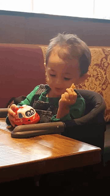 a young boy sitting in a high chair playing with a toy car that says ' 00 ' on it