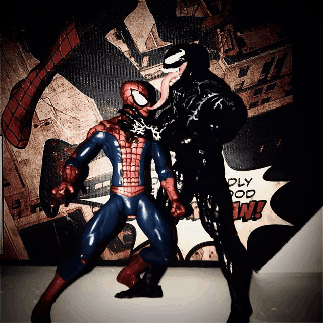 a spider-man and venom action figure standing in front of a comic book cover