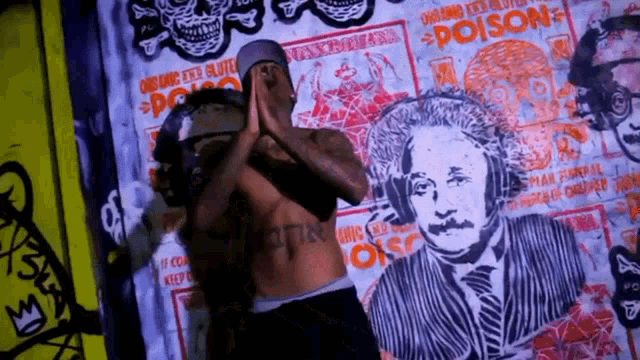 a shirtless man stands in front of a wall with a painting of albert einstein on it