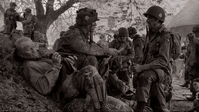 a group of soldiers are gathered under a tree and one of them is wearing a helmet that says 101st airborne