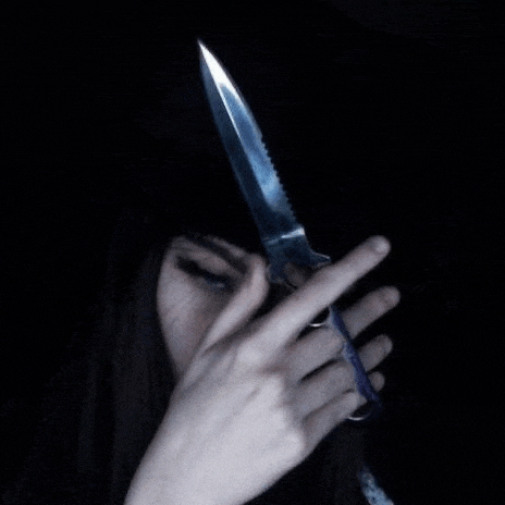 a woman is holding a knife in her hand in front of her face in the dark .