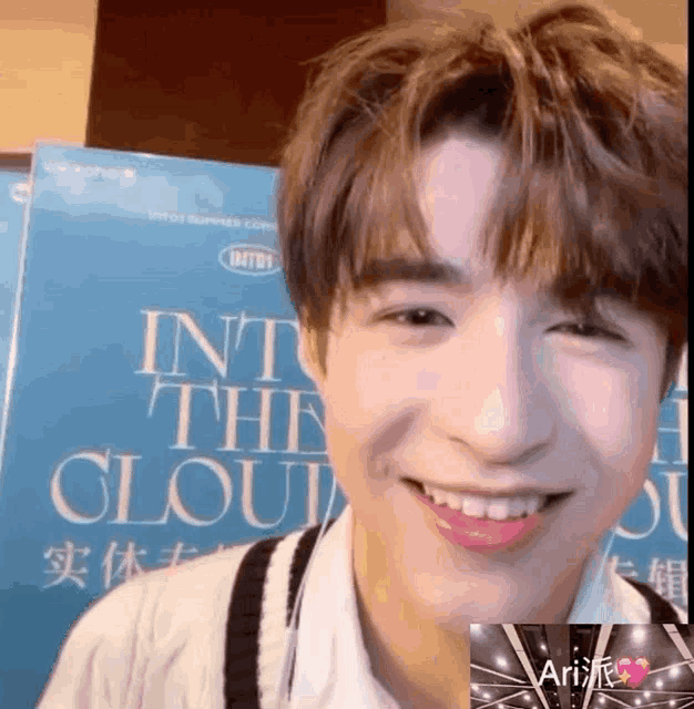 a young man is smiling in front of a sign that says ' into the clouds '