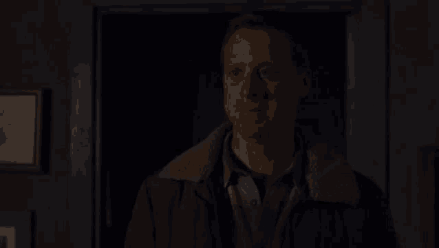 a man is standing in a dark room with a picture on the wall .