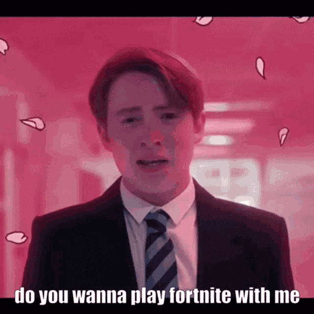 a man in a suit and tie is standing in front of a pink wall and says `` do you wanna play fortnite with me ''