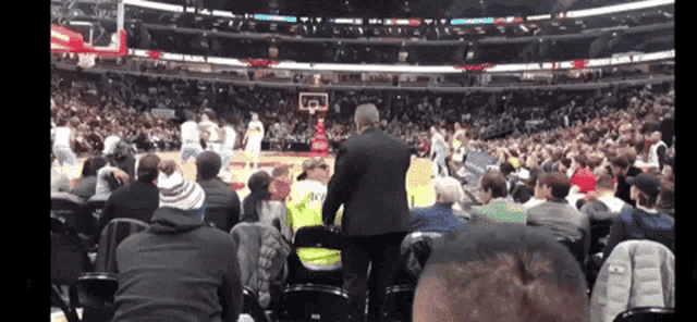 a basketball game is being played in a stadium and a man in a yellow vest stands in the stands