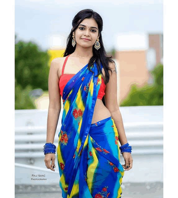 a woman wearing a blue and yellow floral saree and a red top is photographed by raj isaac