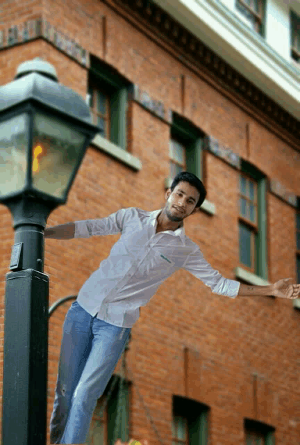 a man is standing on a lamp post with his arms outstretched in front of a brick building