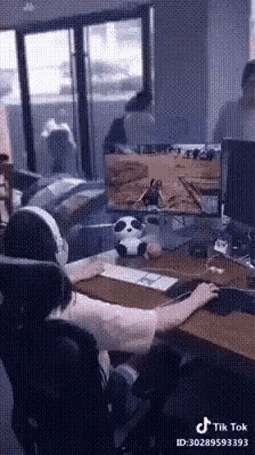 a man is playing a video game on a computer while a panda is sitting on the desk .