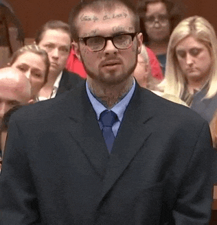 a man in a suit and tie with a tattoo on his face is standing in front of a crowd of people .