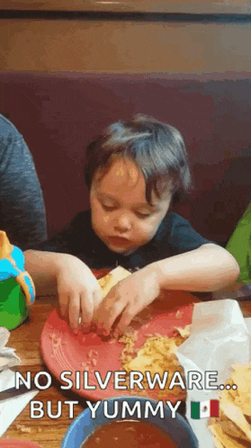 a young boy is sitting at a table with a plate of food and a sign that says no silverware but yummy .