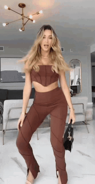 a woman is standing in a living room wearing a brown top and pants