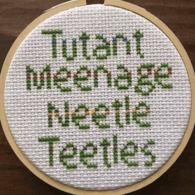 a cross stitch with the words `` mutant teenage mutant turtles '' written on it is in a hoop .