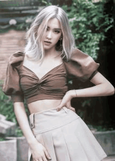 a woman wearing a brown crop top and a beige skirt is standing in front of a tree .