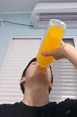 a man is drinking a bottle of orange juice in front of a window