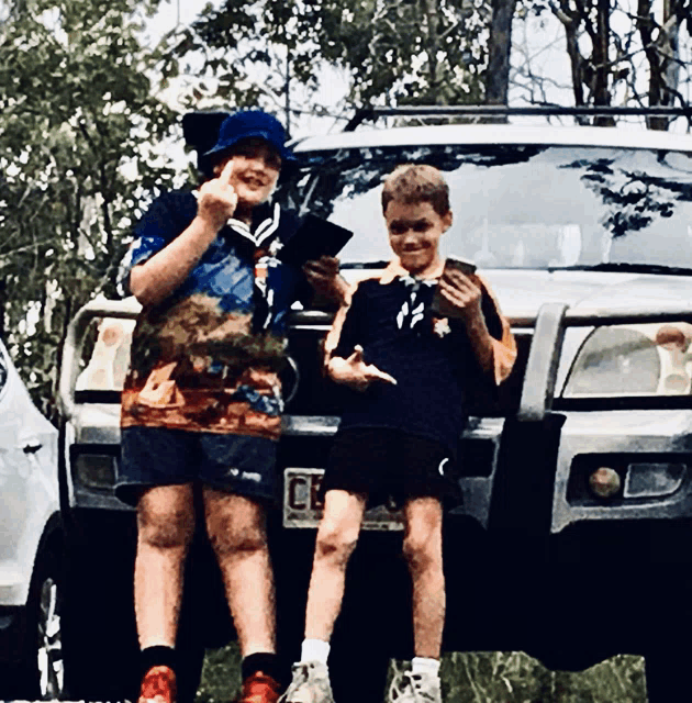 two young boys are standing in front of a car with a license plate that says ' a ' on it