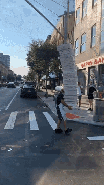 a man is carrying a large stack of pizza boxes down a street in front of a store called happy day