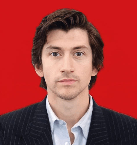 a man with a beard wearing a suit and a white shirt against a red background