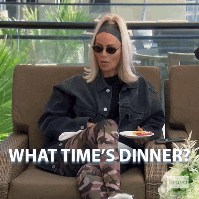 a woman is sitting in a chair with a plate of food and the words " what time 's dinner " behind her