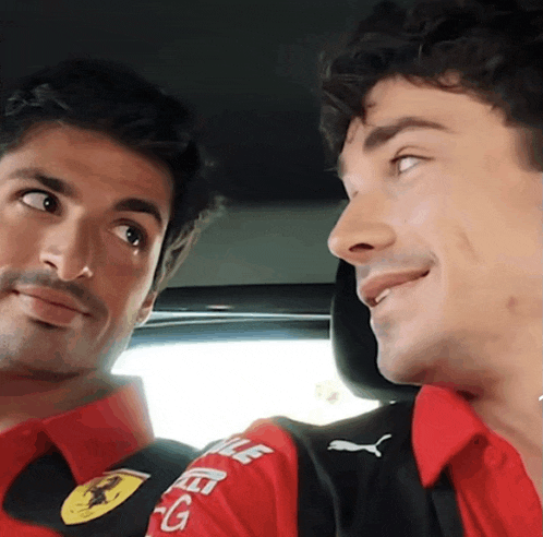 two men are sitting in a car and one has a ferrari shirt on