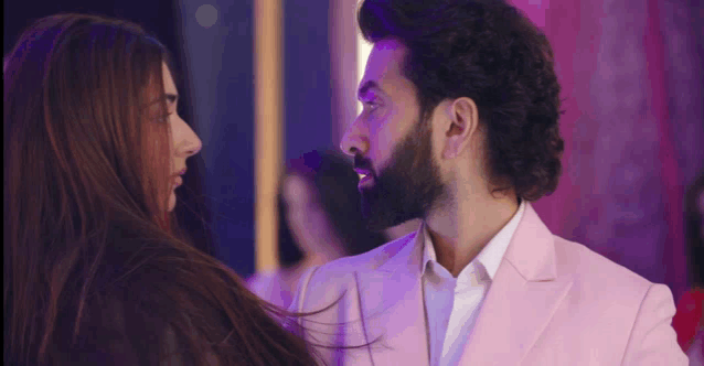 a man with a beard in a pink suit looks at a woman