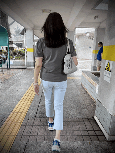 a woman walking down a sidewalk next to a sign that says ' warning '