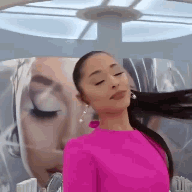 ariana grande is wearing a pink dress and earrings while standing in front of a large painting of herself .