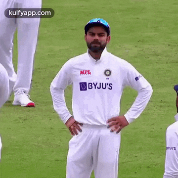 a cricket player is standing on a field with his hands on his hips and looking at the camera .