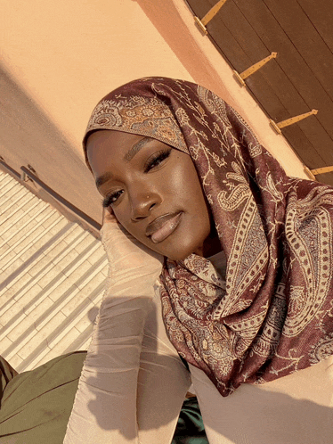 a woman wearing a burgundy paisley scarf looks at the camera