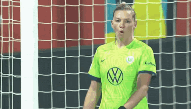 a female soccer player wearing a green shirt with a vw logo on it is standing in front of a goal .