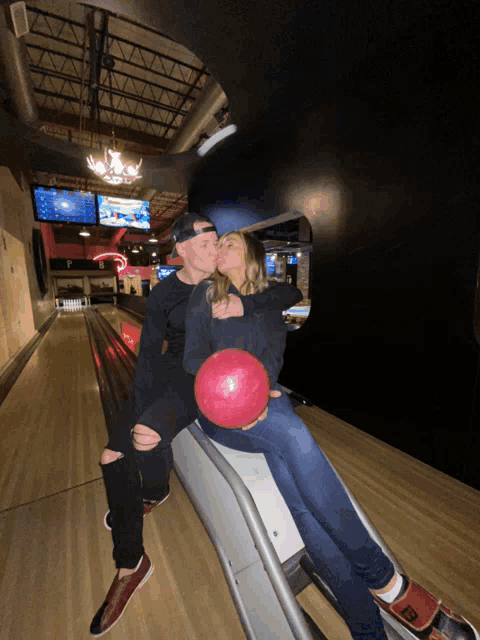 a man and a woman are kissing in a bowling alley and the man is holding a bowling ball with the letter b on it