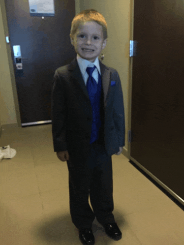 a young boy in a suit and tie stands in front of a hotel door