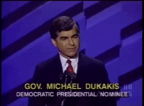 a man in a suit and tie stands in front of a microphone and says gov. michael dukakis democratic presidential nominee