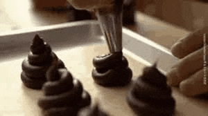 a person is piping chocolate frosting onto a tray of chocolate cupcakes .