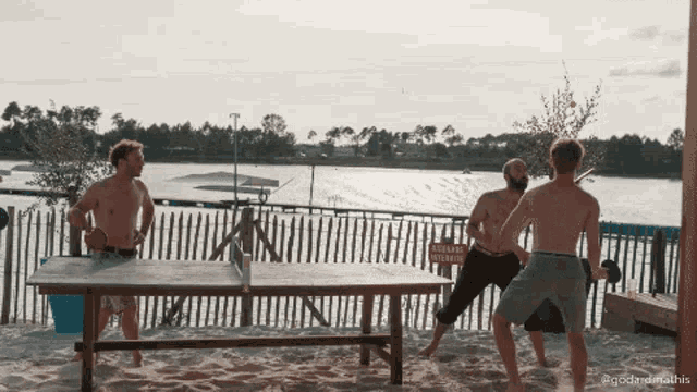 a group of men playing ping pong on a beach with a sign in the background that says " attention vehicule "