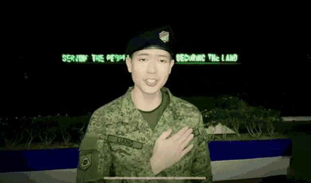 a man in a military uniform is giving a thumbs up in front of a sign that says serve the people .