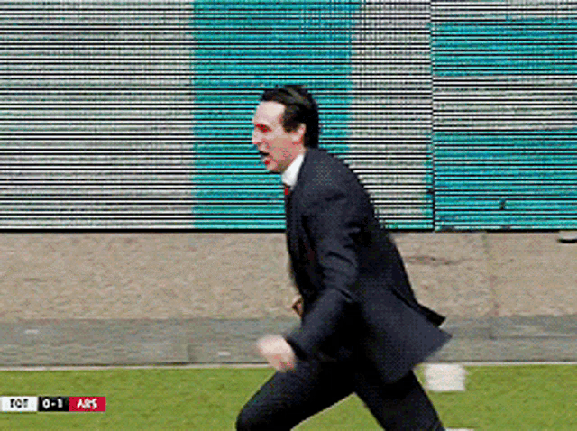 a man in a suit is running on a field with a scoreboard behind him that says tot 0-1 ars