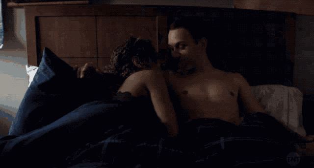 a man and woman kissing on a bed with tnt written on the bottom right