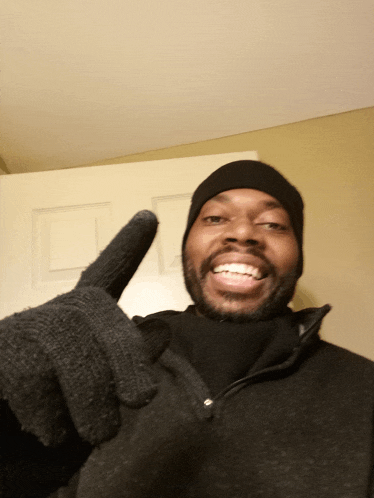 a man wearing a black hat and black gloves is smiling and giving a thumbs up