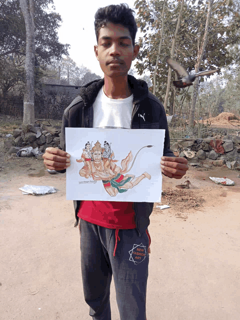 a young man in a puma jacket holds up a drawing of hanuman flying through the air